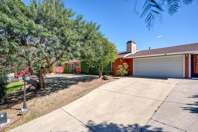 single story home with an attached garage, a chimney, and concrete driveway