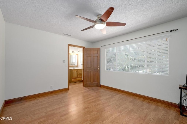 unfurnished room featuring baseboards, visible vents, light wood-style flooring, and a textured ceiling