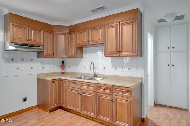 kitchen featuring under cabinet range hood, light wood-style flooring, visible vents, and a sink