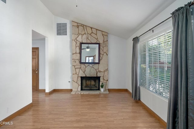 living area featuring light wood-style flooring, visible vents, a wealth of natural light, and a stone fireplace