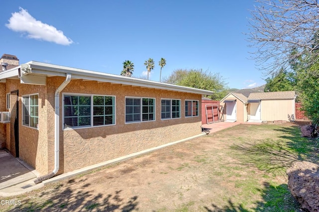 rear view of property with an outbuilding, a yard, a chimney, and stucco siding