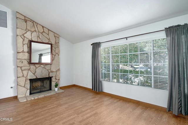 unfurnished living room featuring visible vents, vaulted ceiling, a stone fireplace, wood finished floors, and baseboards