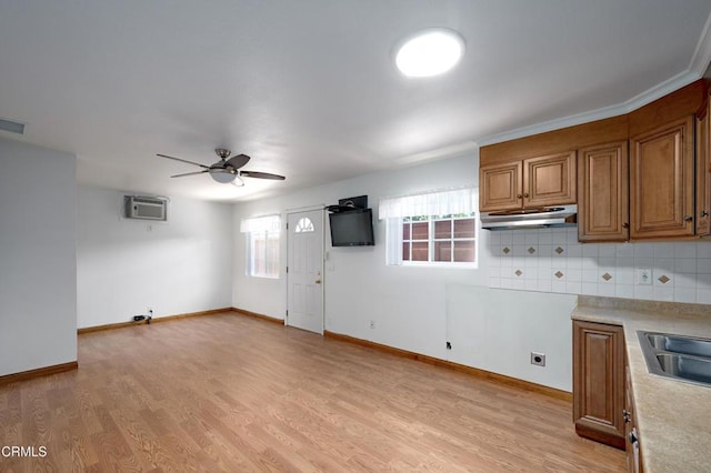 kitchen with light wood-style floors, brown cabinetry, a wall mounted AC, and under cabinet range hood