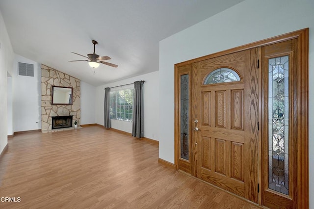 foyer entrance with visible vents, light wood-style flooring, ceiling fan, a stone fireplace, and vaulted ceiling