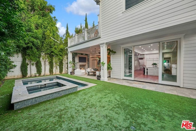 back of property featuring a lawn, an outdoor stone fireplace, a patio area, a balcony, and an in ground hot tub