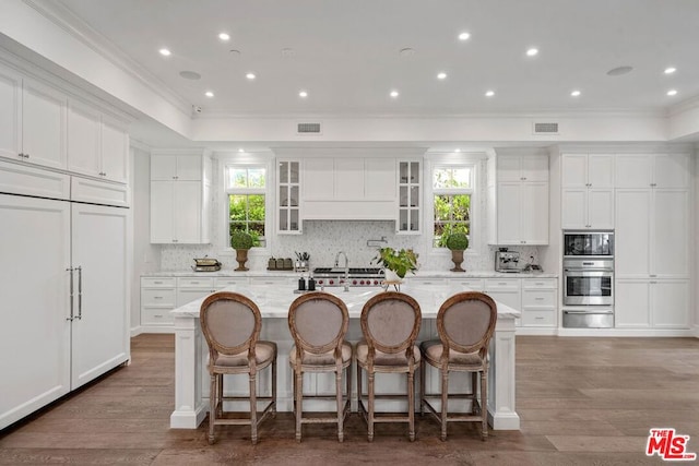 kitchen with a breakfast bar, white cabinets, a kitchen island with sink, light stone counters, and a healthy amount of sunlight