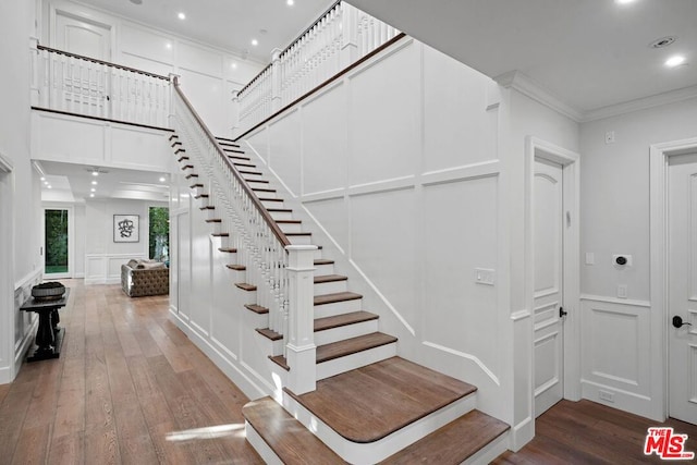 stairs with hardwood / wood-style flooring, ornamental molding, and a towering ceiling