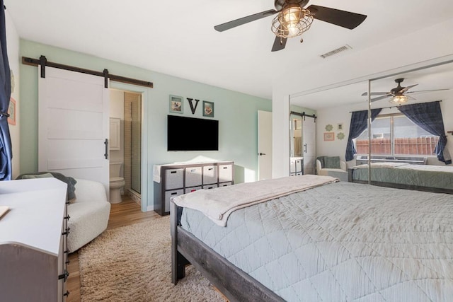 bedroom featuring ceiling fan, connected bathroom, a barn door, and light wood-type flooring