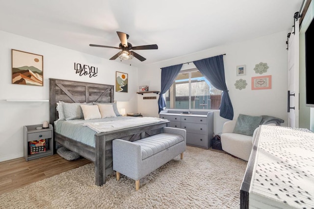 bedroom with light hardwood / wood-style flooring, a barn door, and ceiling fan