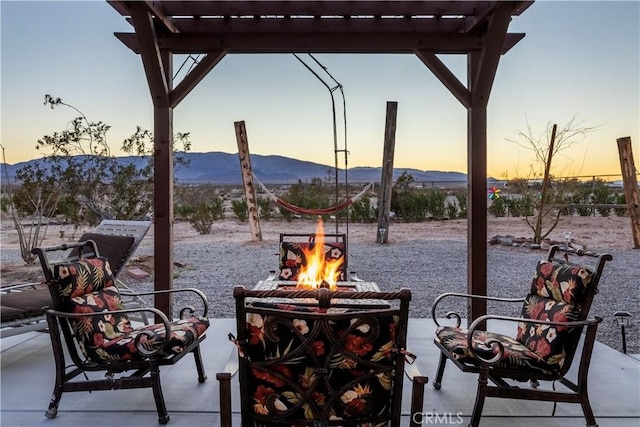 patio terrace at dusk with a pergola, a mountain view, and a fire pit