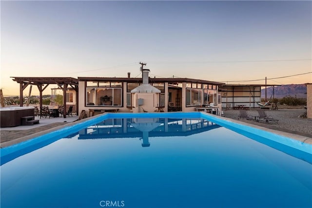 pool at dusk featuring a hot tub, a patio, and a pergola