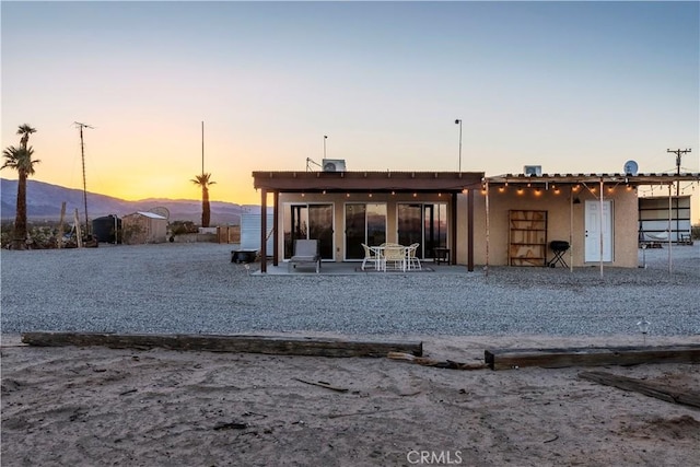 back house at dusk featuring a mountain view and a patio area