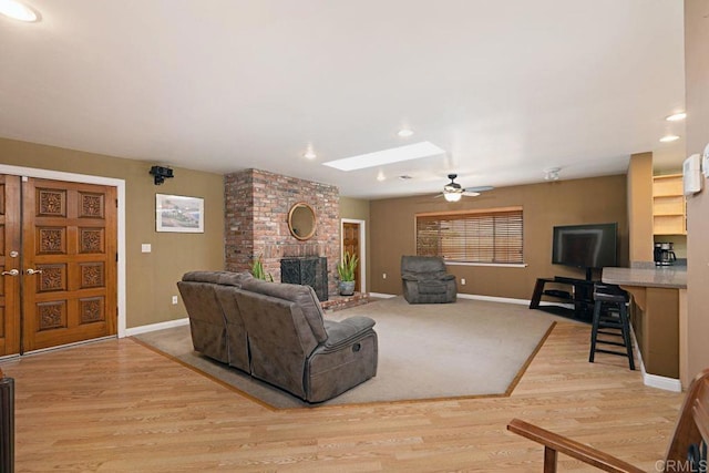 living room featuring light hardwood / wood-style flooring, a fireplace, a skylight, and ceiling fan