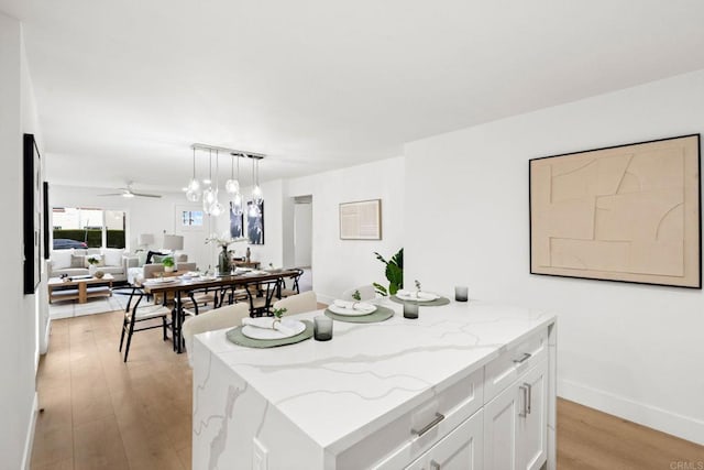 kitchen with light hardwood / wood-style flooring, a kitchen island, pendant lighting, light stone countertops, and white cabinets