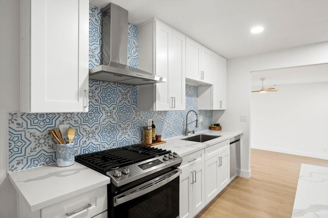 kitchen featuring wall chimney range hood, sink, white cabinets, and appliances with stainless steel finishes