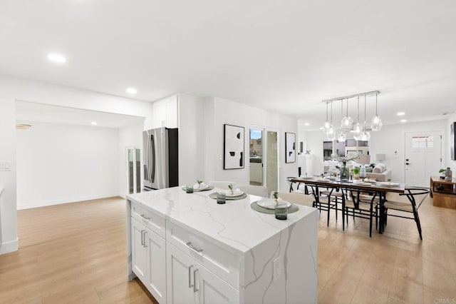 kitchen with stainless steel refrigerator with ice dispenser, light stone counters, light hardwood / wood-style flooring, a kitchen island, and white cabinets