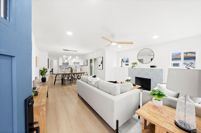 living room featuring a tiled fireplace, a healthy amount of sunlight, ceiling fan, and light wood-type flooring