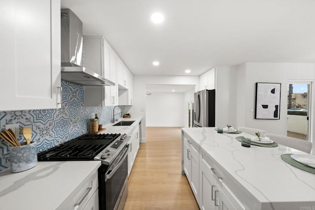 kitchen with appliances with stainless steel finishes, sink, wall chimney range hood, and white cabinets