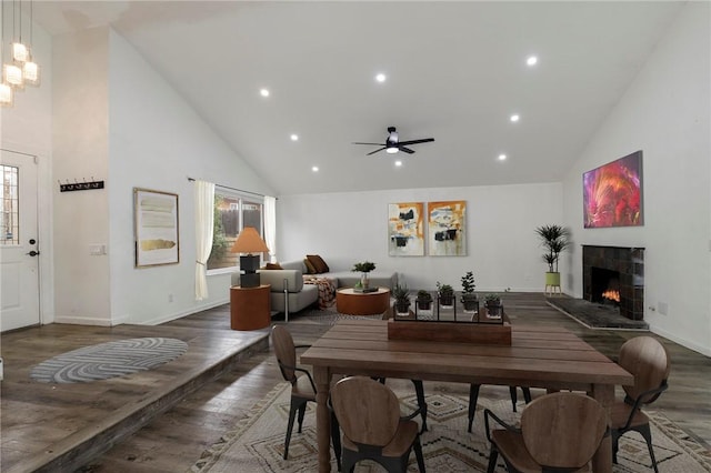 dining area featuring dark hardwood / wood-style floors, a tiled fireplace, and high vaulted ceiling