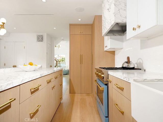 kitchen featuring high end stainless steel range oven, light brown cabinetry, light stone countertops, and light hardwood / wood-style flooring