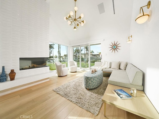 living room featuring high vaulted ceiling, hardwood / wood-style floors, a notable chandelier, and a fireplace