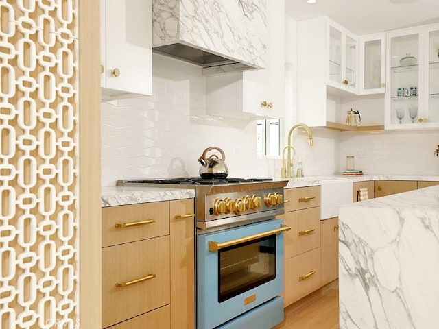 kitchen featuring light stone counters, backsplash, high end stainless steel range oven, and premium range hood