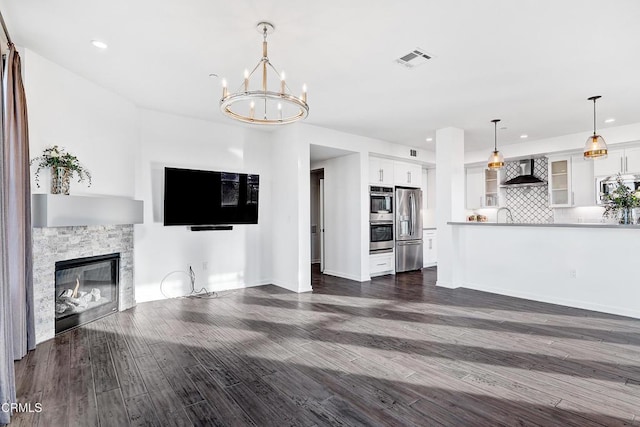 unfurnished living room with a stone fireplace, dark hardwood / wood-style floors, and a chandelier