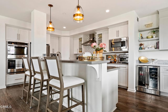 kitchen featuring wall chimney range hood, appliances with stainless steel finishes, hanging light fixtures, wine cooler, and white cabinets