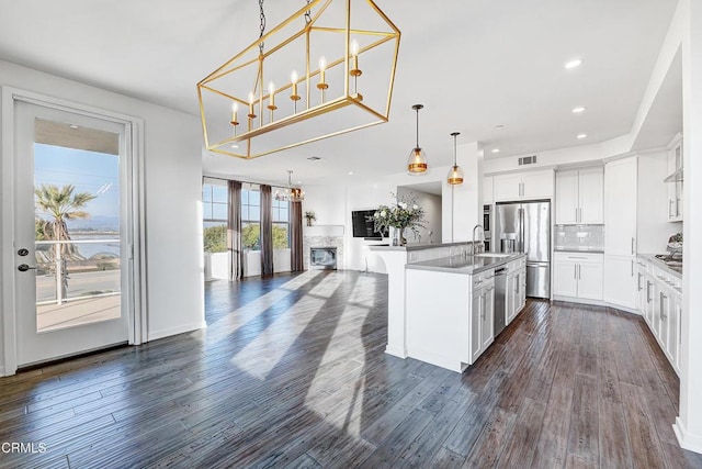 kitchen with decorative light fixtures, white cabinetry, sink, stainless steel fridge, and a center island with sink