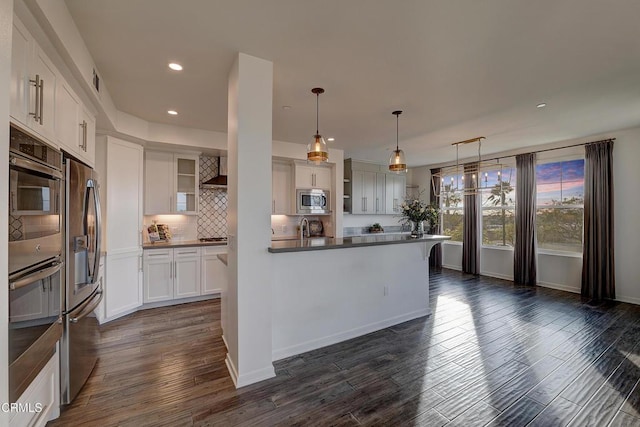 kitchen featuring appliances with stainless steel finishes, white cabinetry, hanging light fixtures, backsplash, and dark hardwood / wood-style flooring