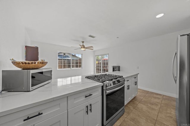 kitchen with light stone counters, appliances with stainless steel finishes, light tile patterned floors, and white cabinets