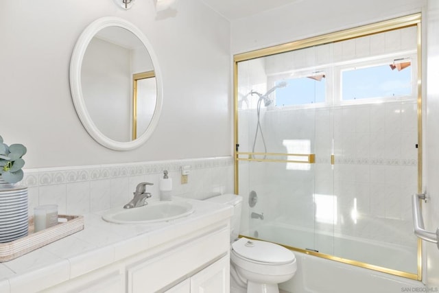 full bathroom featuring bath / shower combo with glass door, tile walls, vanity, and toilet