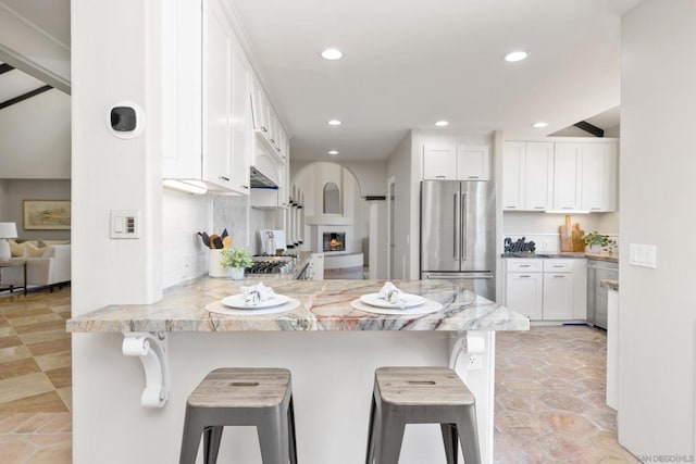 kitchen featuring high end fridge, white cabinets, a kitchen breakfast bar, and kitchen peninsula