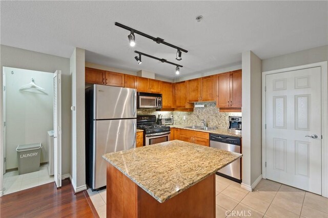 kitchen with sink, appliances with stainless steel finishes, a center island, light stone counters, and decorative backsplash