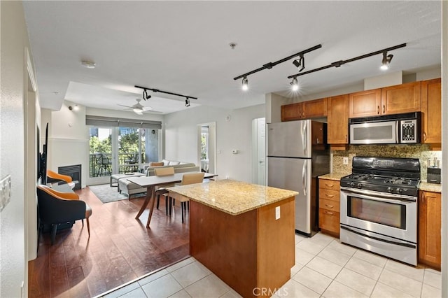 kitchen with light tile patterned floors, appliances with stainless steel finishes, ceiling fan, light stone countertops, and backsplash