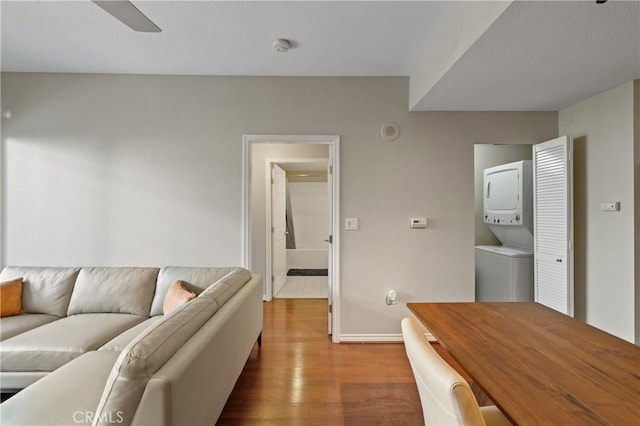 living room with stacked washer / drying machine, hardwood / wood-style flooring, and ceiling fan