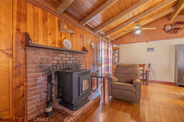 living room with vaulted ceiling with beams, hardwood / wood-style flooring, wooden walls, and a wood stove