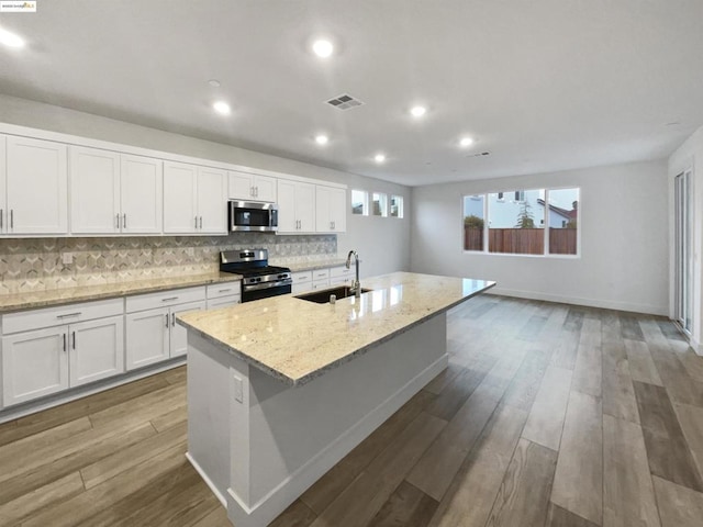 kitchen with light stone counters, stainless steel appliances, an island with sink, and white cabinets