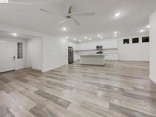 kitchen with stainless steel appliances, tasteful backsplash, light hardwood / wood-style floors, an island with sink, and white cabinets