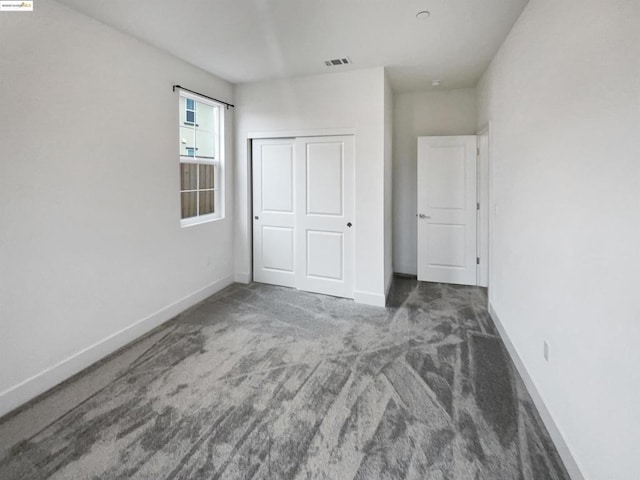 unfurnished bedroom with dark colored carpet and a closet