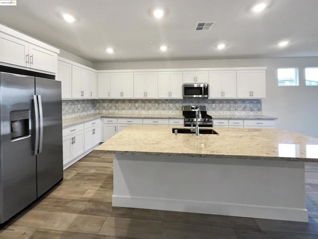 kitchen featuring a kitchen island with sink, light stone counters, white cabinets, and appliances with stainless steel finishes