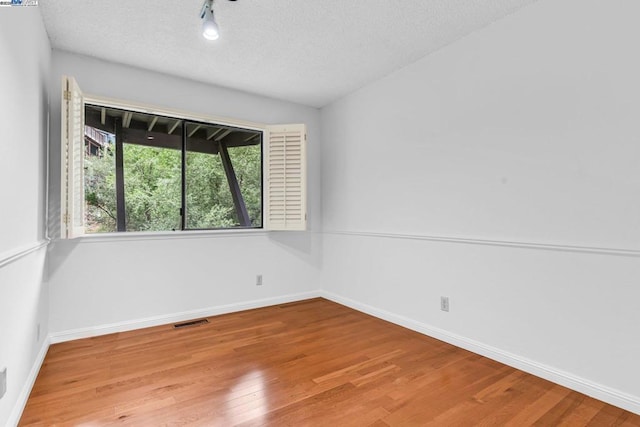 unfurnished room with track lighting, light hardwood / wood-style floors, and a textured ceiling