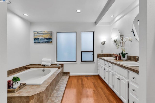 bathroom featuring vanity, a relaxing tiled tub, and wood-type flooring