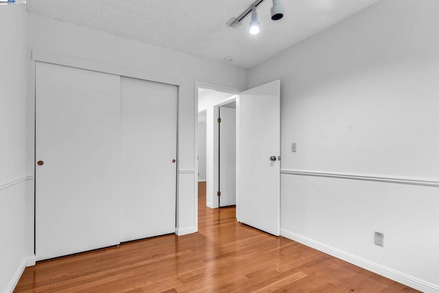 unfurnished bedroom featuring hardwood / wood-style flooring, track lighting, a closet, and a textured ceiling