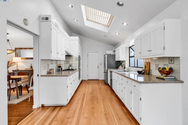 kitchen featuring sink, lofted ceiling with skylight, white cabinets, dark stone counters, and light wood-type flooring