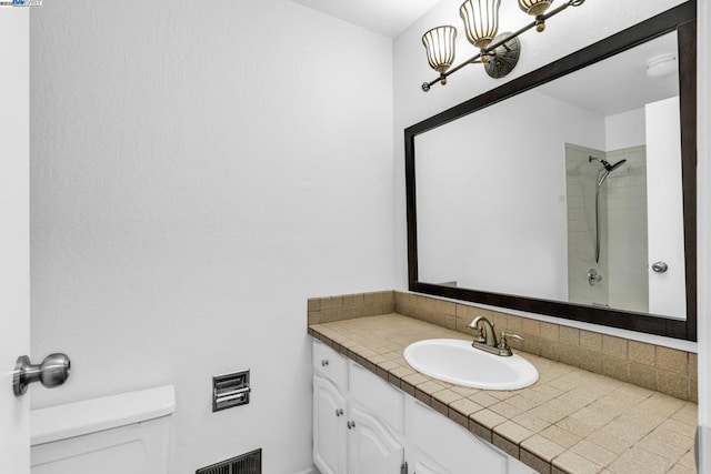 bathroom with a tile shower, backsplash, vanity, and toilet