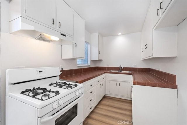 kitchen with tile countertops, white cabinetry, sink, white gas range oven, and light hardwood / wood-style flooring