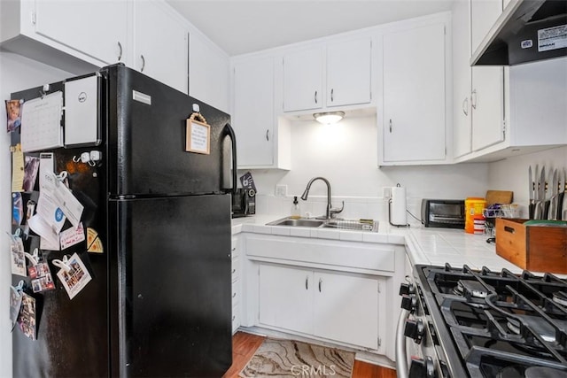 kitchen with white cabinetry, sink, stainless steel range with gas cooktop, and black fridge