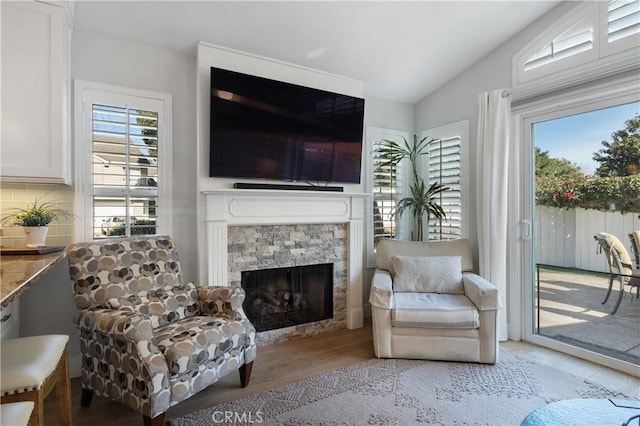 sitting room with lofted ceiling, a stone fireplace, light hardwood / wood-style flooring, and a healthy amount of sunlight