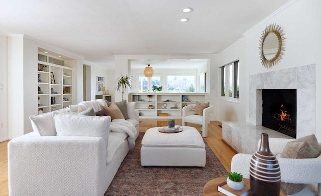 living room featuring built in shelves, ornamental molding, wood-type flooring, and a high end fireplace